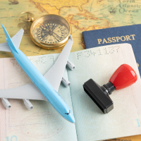 Travel essentials including a toy airplane, a passport, a small model airplane, a stamp, a compass, and a boarding pass on a table.