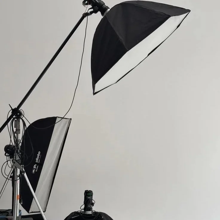 Photography studio setup with large umbrella lights and softboxes on a plain white wall background.