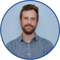 Portrait of a man with a beard and mustache, wearing a blue checkered shirt, smiling against a light blue background with a dark blue oval border.