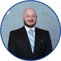 Headshot of a smiling man wearing a suit and tie, against a blue background with a marble wall pattern.