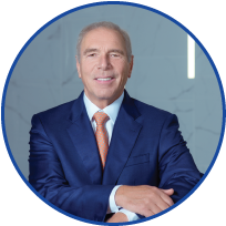 Professional man in a navy blue suit and orange tie, smiling with arms crossed, in a modern office setting.