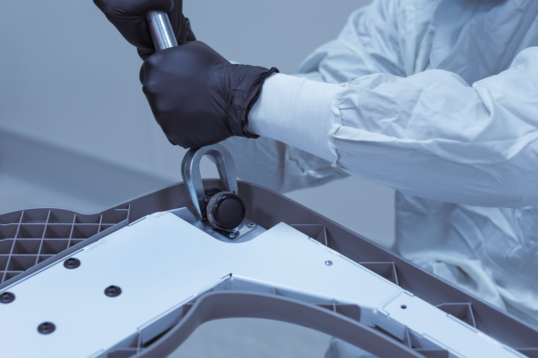 A person wearing black gloves and a white lab coat working on a piece of electronic equipment, using a metal tool to adjust a component.