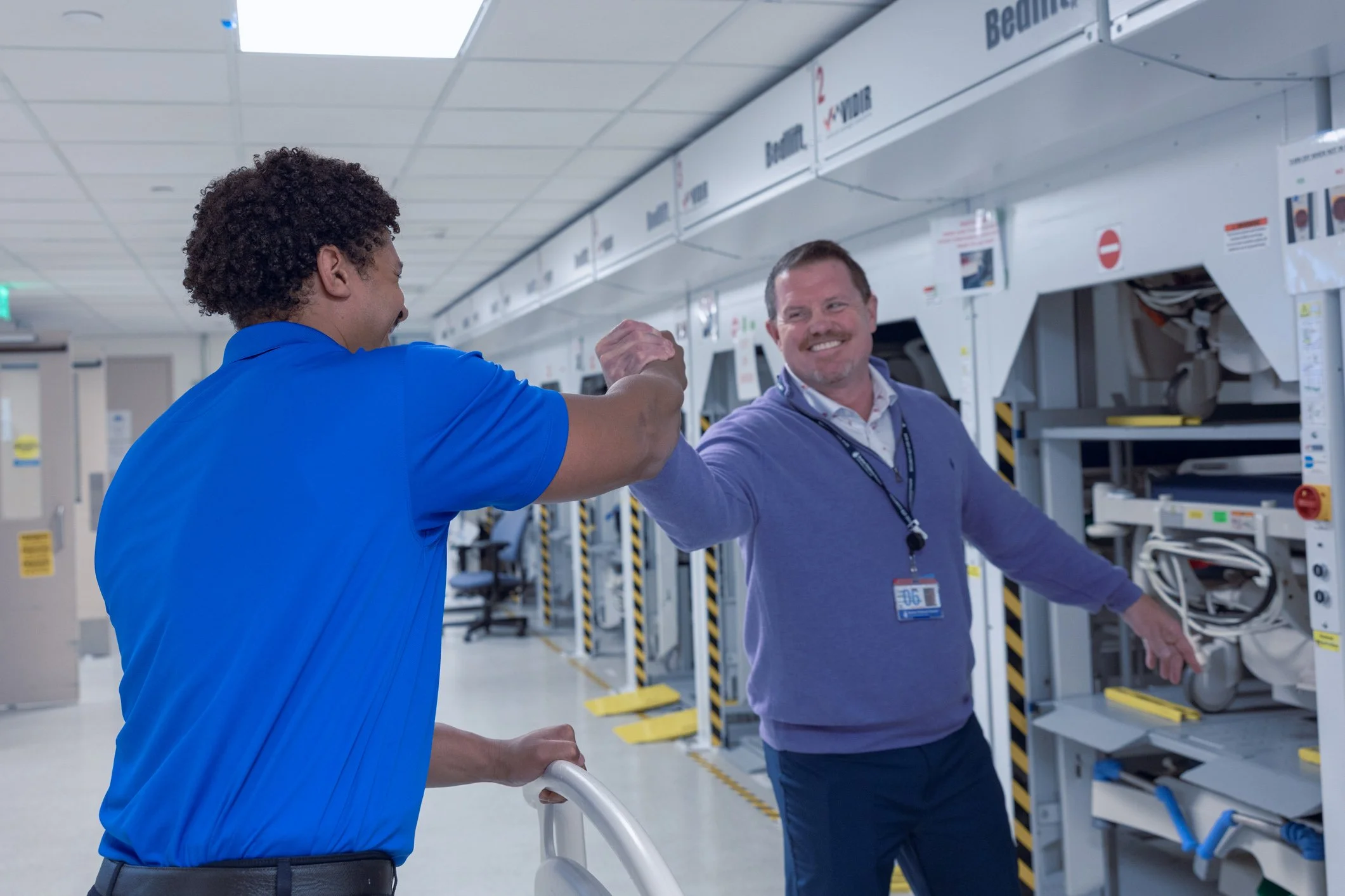 Two men in a laundry or industrial setting, shaking hands and smiling.
