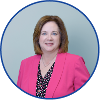Portrait of a woman with shoulder-length brown hair, wearing a pink blazer and a black and white polka dot blouse, smiling against a light blue background.