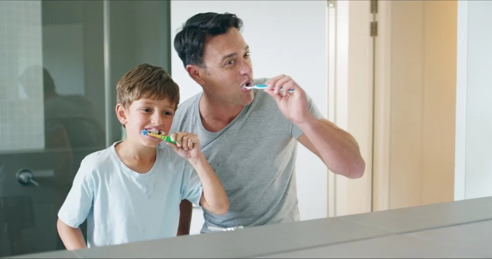 A man and a young boy brushing their teeth together in a bathroom.