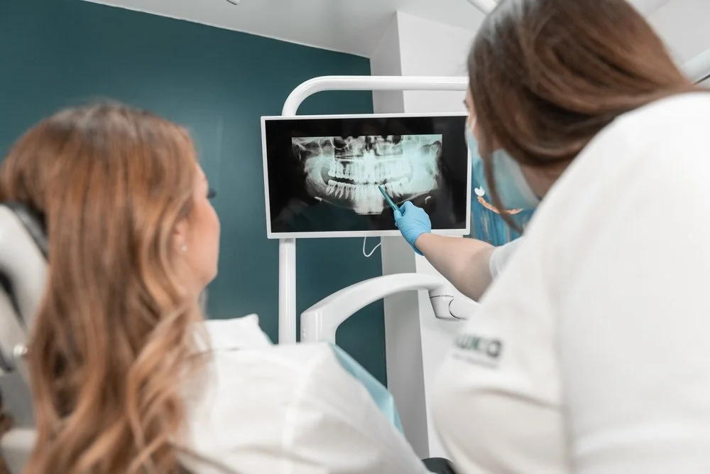 Dentist shows a dental X-ray of a patient's teeth on a monitor during a consultation.