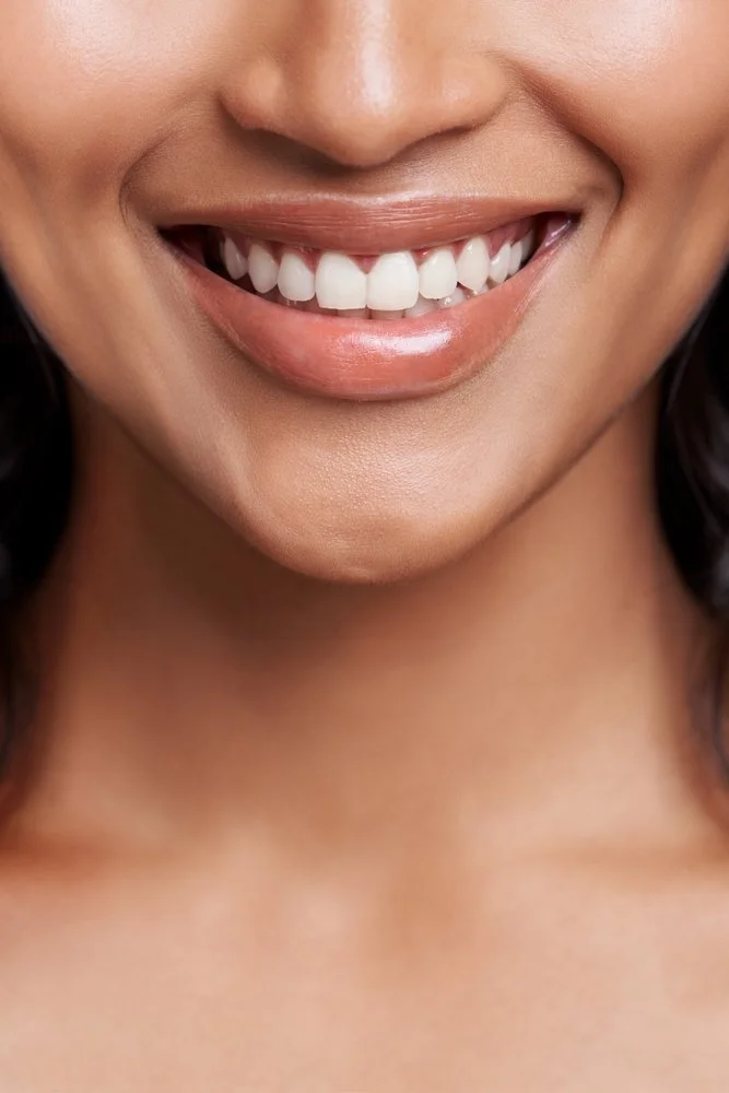 Close-up of a person's smiling mouth showing white teeth, lips slightly parted, and smooth skin.