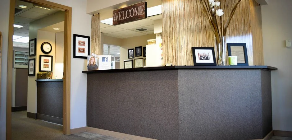 Reception desk in an office with framed pictures, a 'WELCOME' sign overhead, and decorative plants.