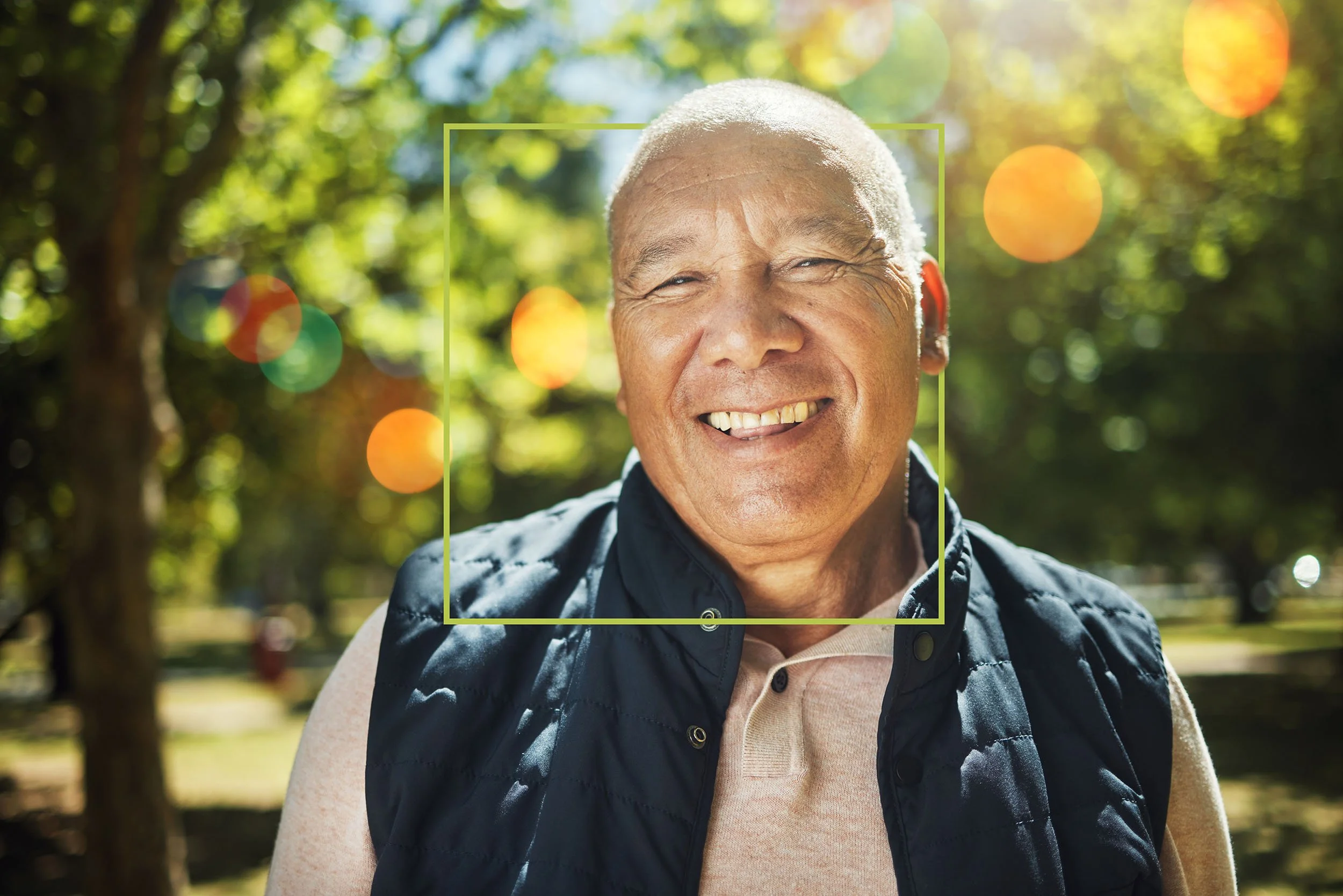 Smiling elderly man outdoors with sunlight and trees in the background.