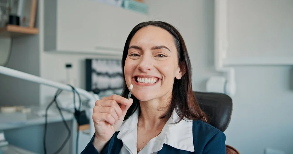 A woman in a dentist's office smiling while holding dental instrument.