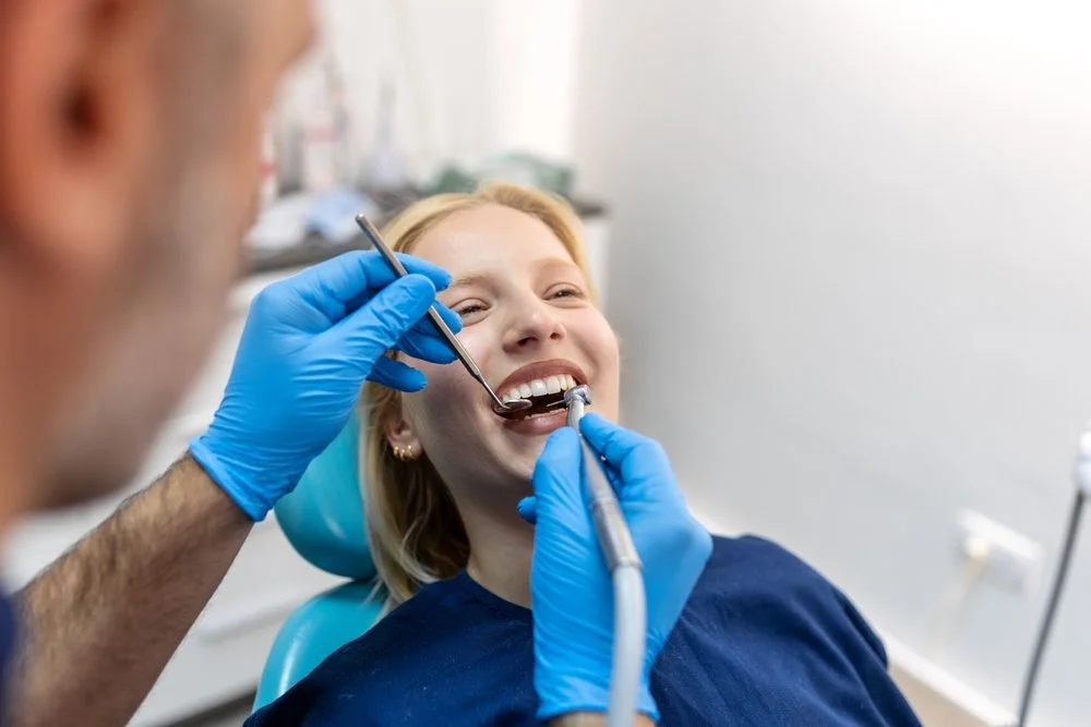 A woman smiling while receiving dental treatment from a dentist in a dental office.