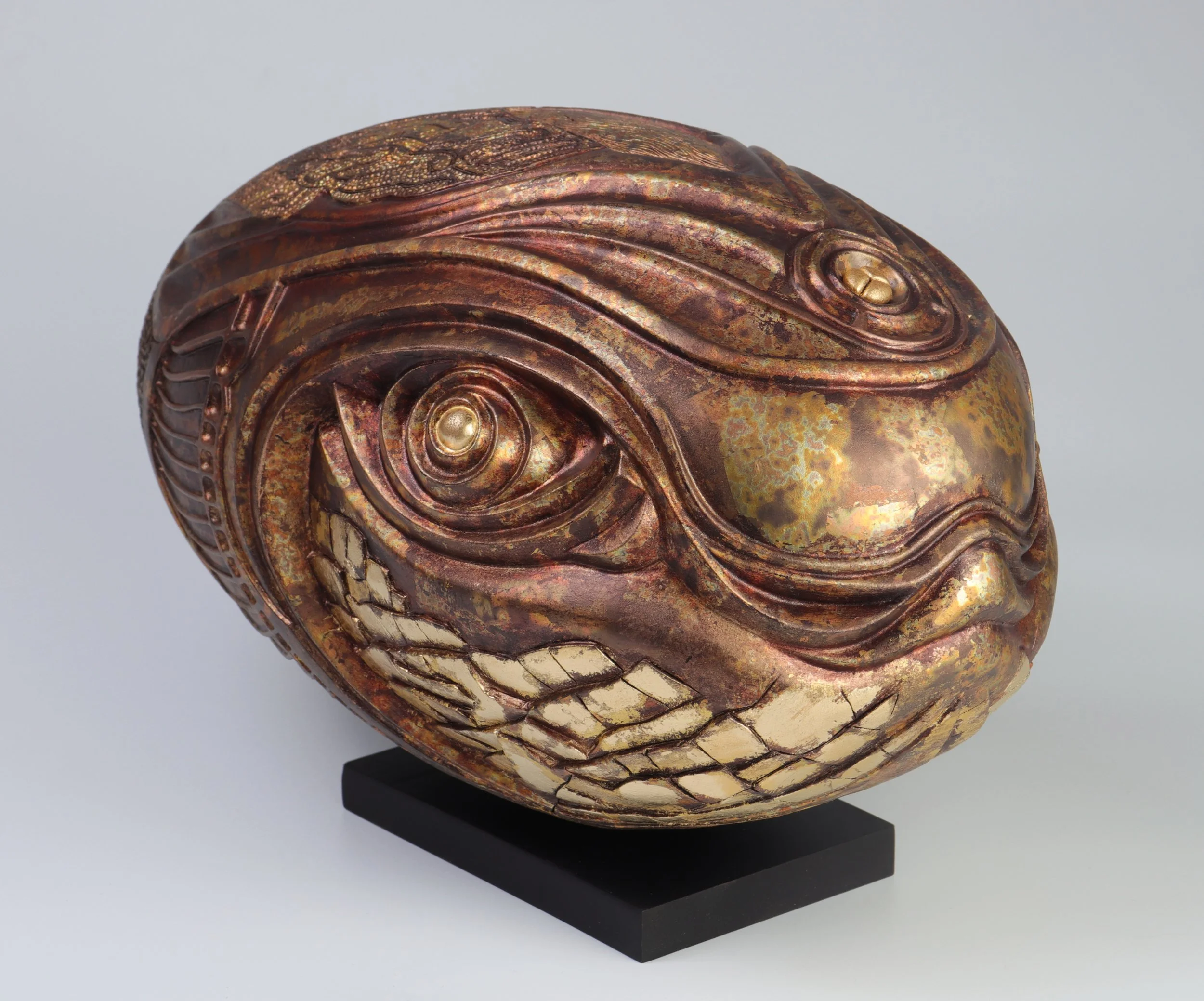 Aged metallic sculpture with intricate details and a textured surface, displayed on a black base.