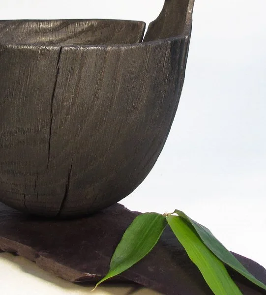 Close-up of scorched wooden bowl, partially visible, bamboo leaves, on slate plinth.