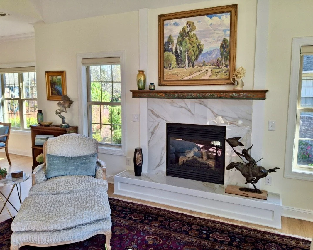 A kitchen with brown cabinets, a white marble countertop, a light green tiled backsplash, and decorative items on the counter and in the glass-front cabinets.