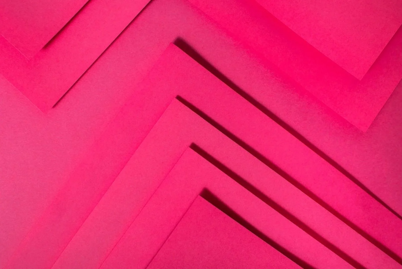 A bright pink geometric pattern that looks like layered paper forming  chevron pattern