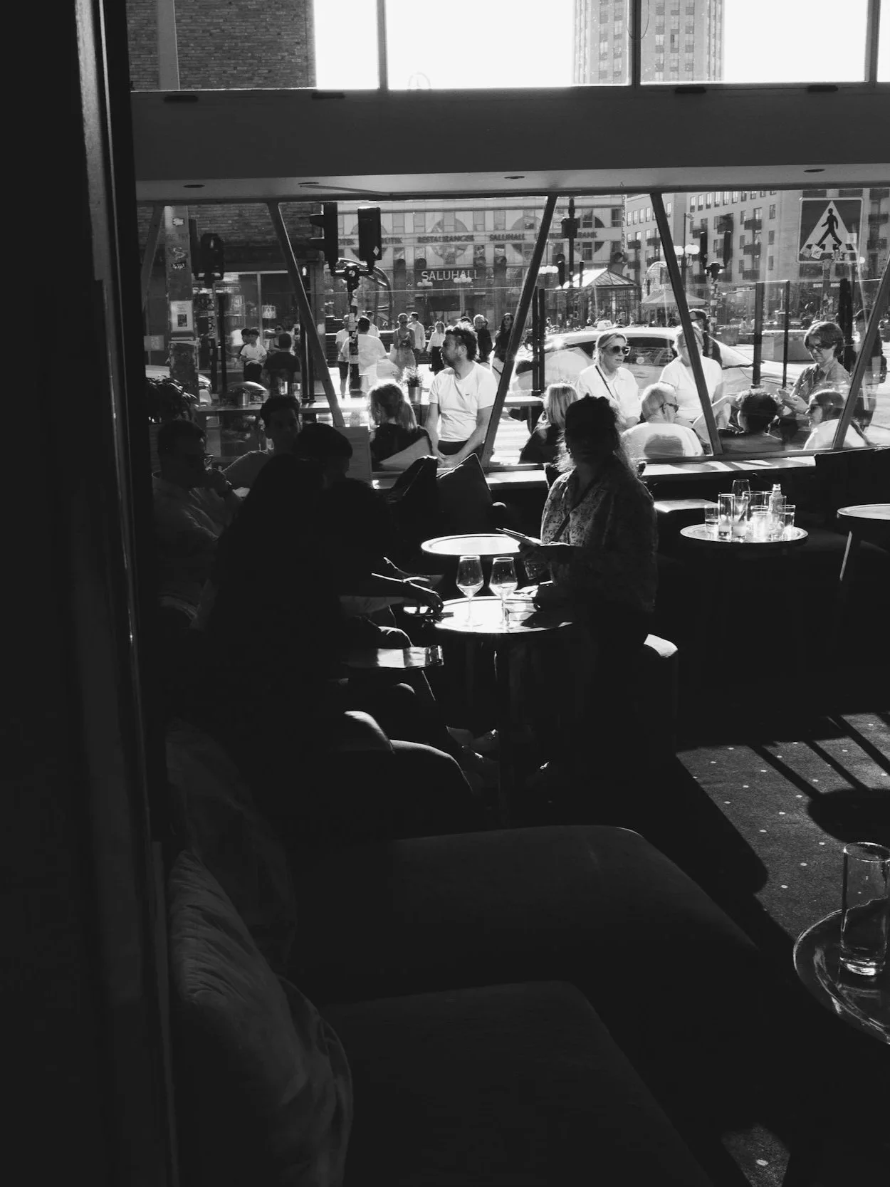 People sitting at tables inside a restaurant, with large windows showing a busy street scene with pedestrians and buildings outside.