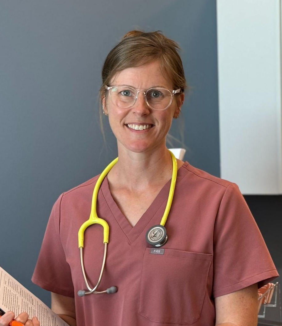 A female healthcare professional in scrubs, wearing glasses, with a yellow stethoscope around her neck, smiling and holding a document.