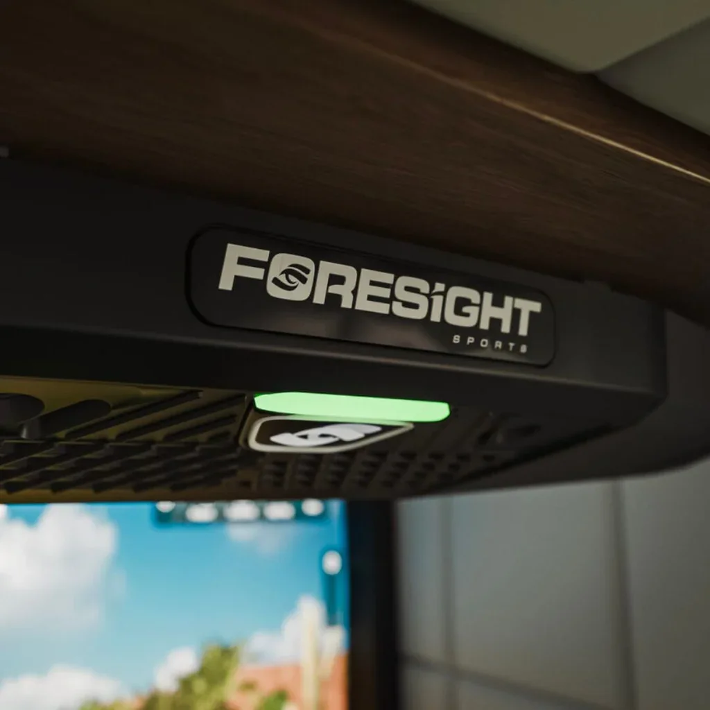Close-up of a Foresight Sports device with a green indicator light, mounted under a wooden surface.