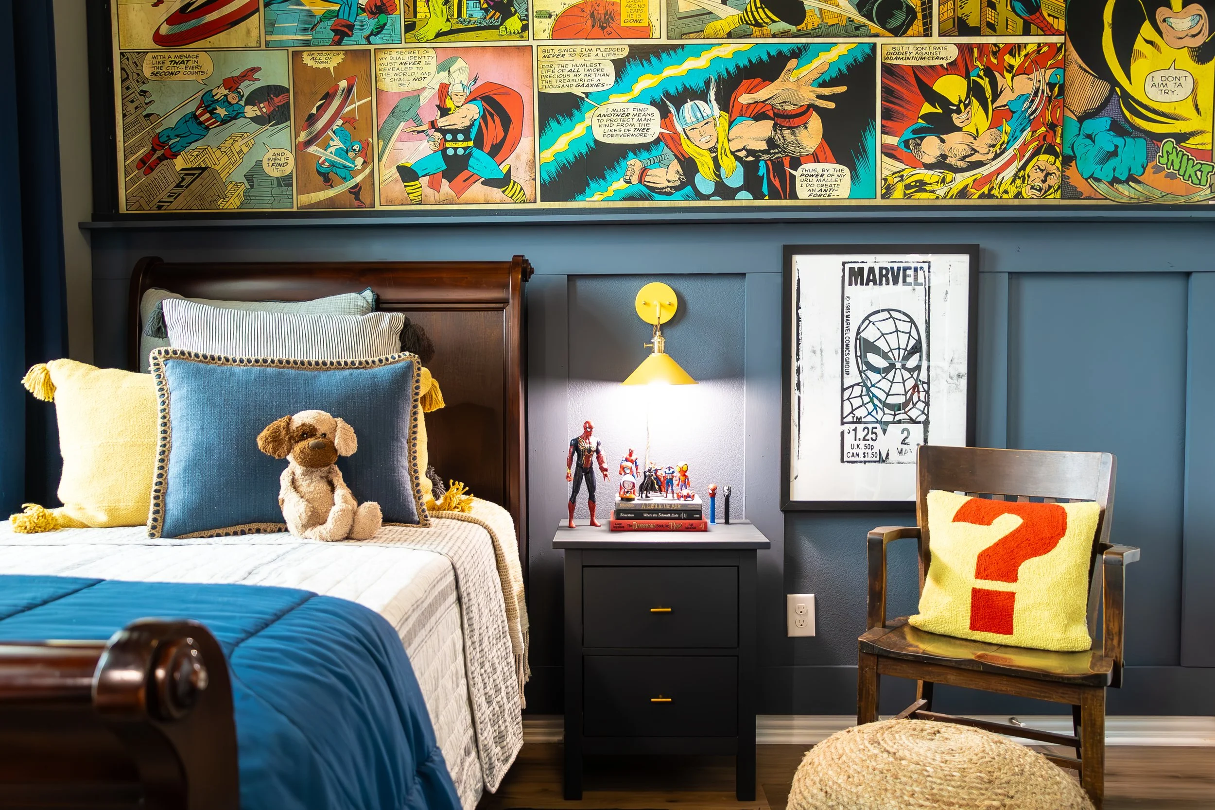 Bedroom with Marvel comic artwork on the wall and various superhero toys and decorations, including a Teddy bear on the bed and a wooden chair with a colorful cushion.