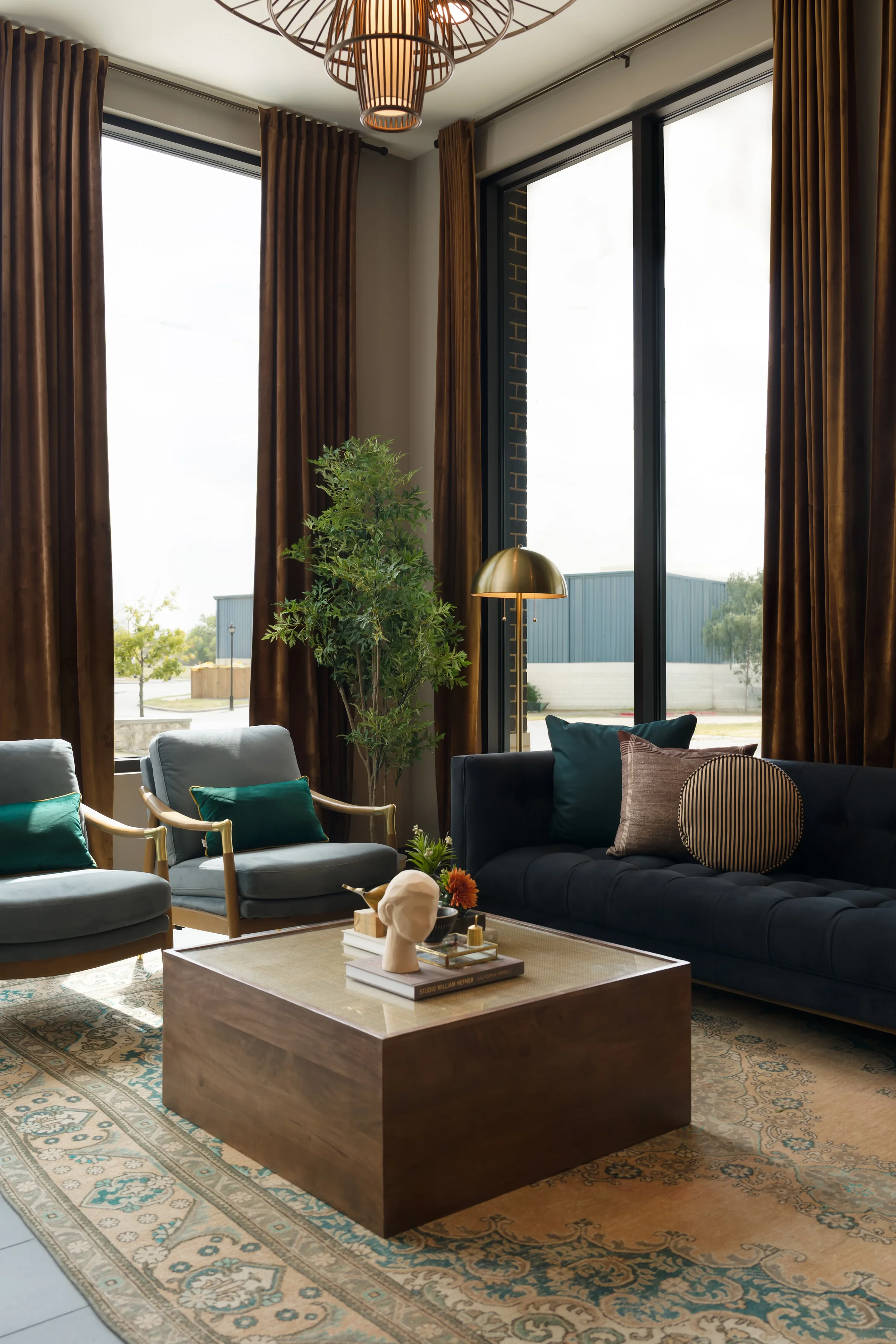 Seating area at The Platform in Frisco, Texas, with brown velvet drapes, teal armchairs, a navy tufted sofa, and a layered rug, designed by Artbuckle & Co.