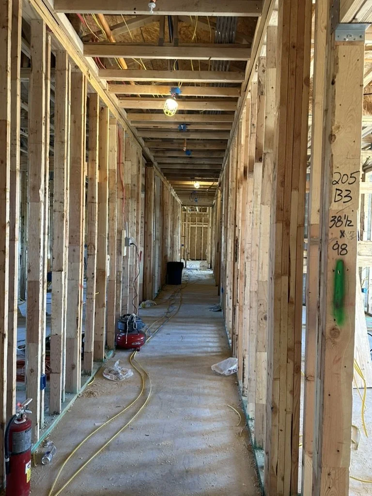 Raw wood stud framing and electrical wiring phase for the resident entry corridor at Beacon in Frisco, Texas, with site oversight by Artbuckle & Co.