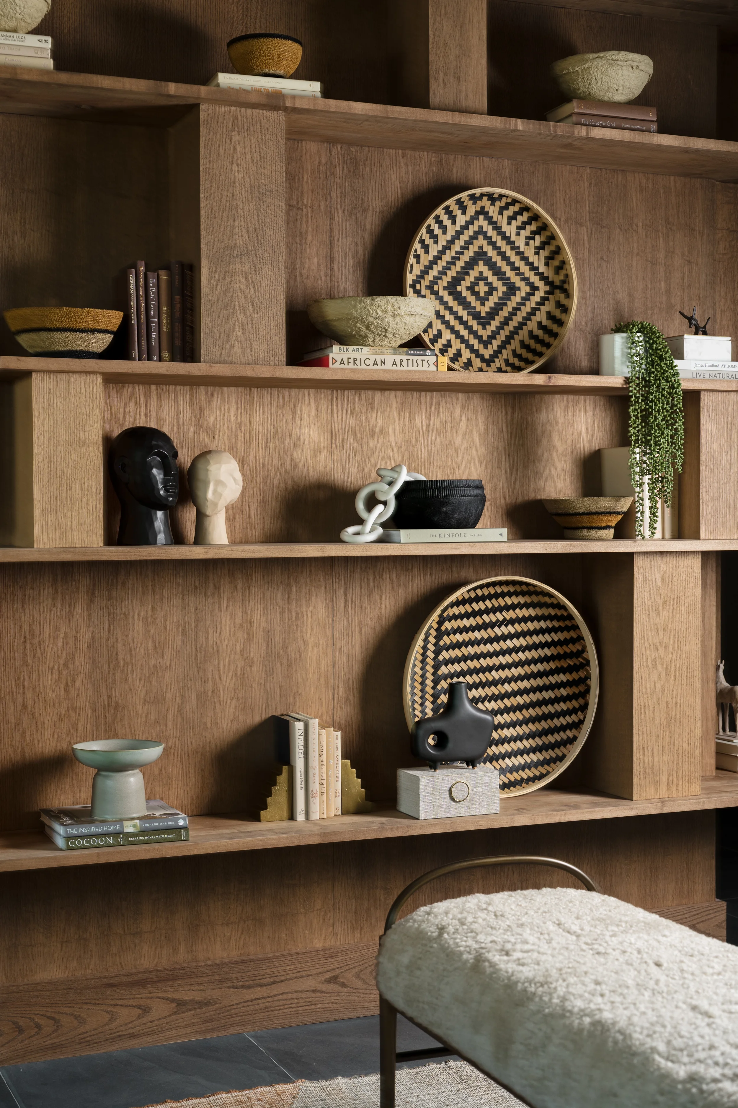 Layered walnut shelves with woven baskets, sculptural busts, and books at The View in Frisco, Texas, designed by Artbuckle & Co.