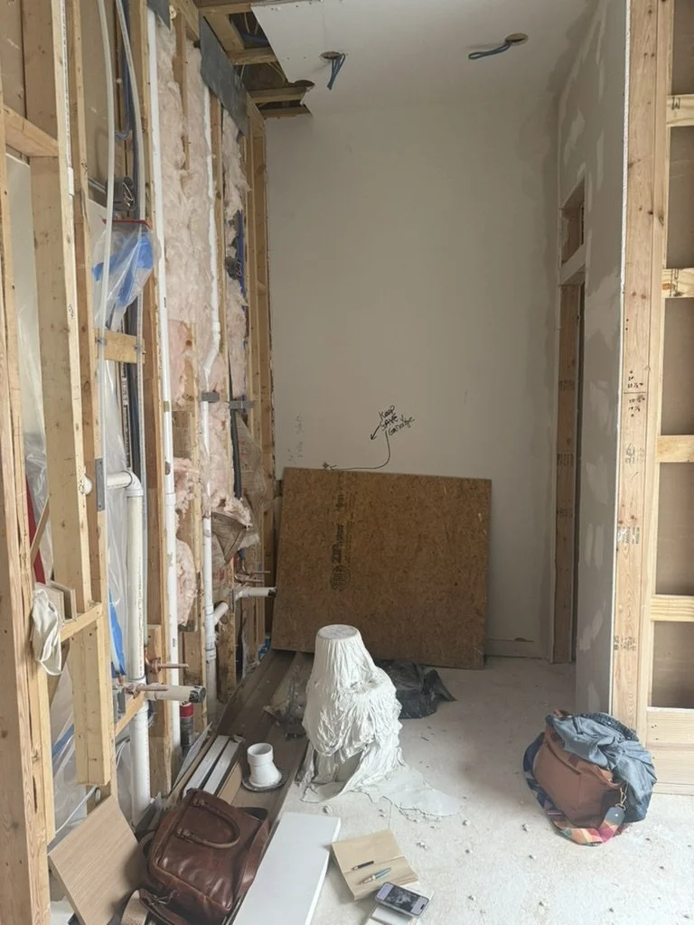 During construction: a primary bathroom wall opened to the studs, with insulation and plumbing exposed, in a Lakewood Hills home in Dallas, Texas, on the Artbuckle & Co. renovation.