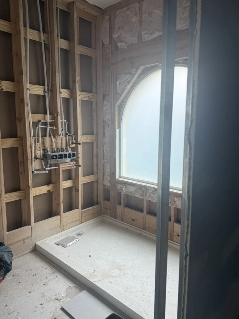 During construction: the primary bathroom shower framed to the studs in a Lakewood Hills home in Dallas, Texas, with exposed plumbing, a new shower base, and an arched window, on the Artbuckle & Co. renovation.