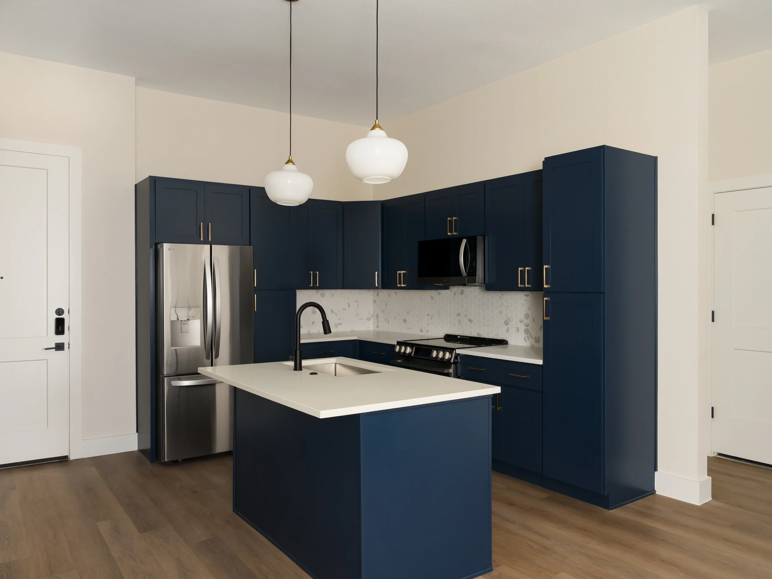 Apartment kitchen at The View in Frisco's Rail District with navy cabinetry, island and glass pendants. Designed by Artbuckle & Co.