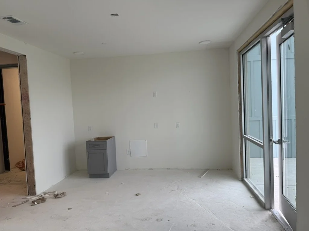 Before view of the resident amenity lounge during construction at East 9th apartments in Dallas, Texas, showing unpainted drywall, bare concrete subfloor, and exposed window framing before interior buildout by Artbuckle & Co.