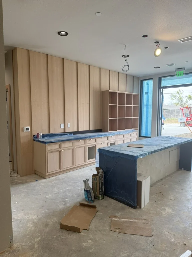 Amenity kitchen under construction at The View in Frisco's Rail District with oak cabinetry and paneled walls. Designed by Artbuckle & Co.