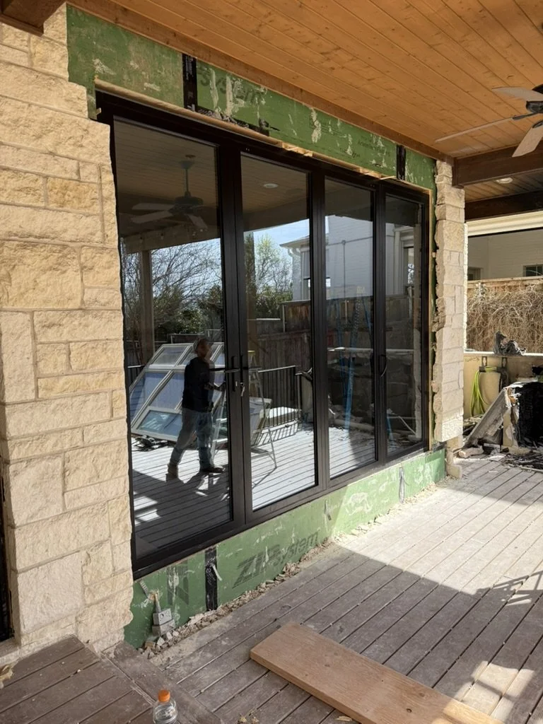 During construction: a large black-framed glass door system installed in a stone exterior wall at the back of a Lakewood Hills home in Dallas, Texas, on the Artbuckle & Co. renovation.