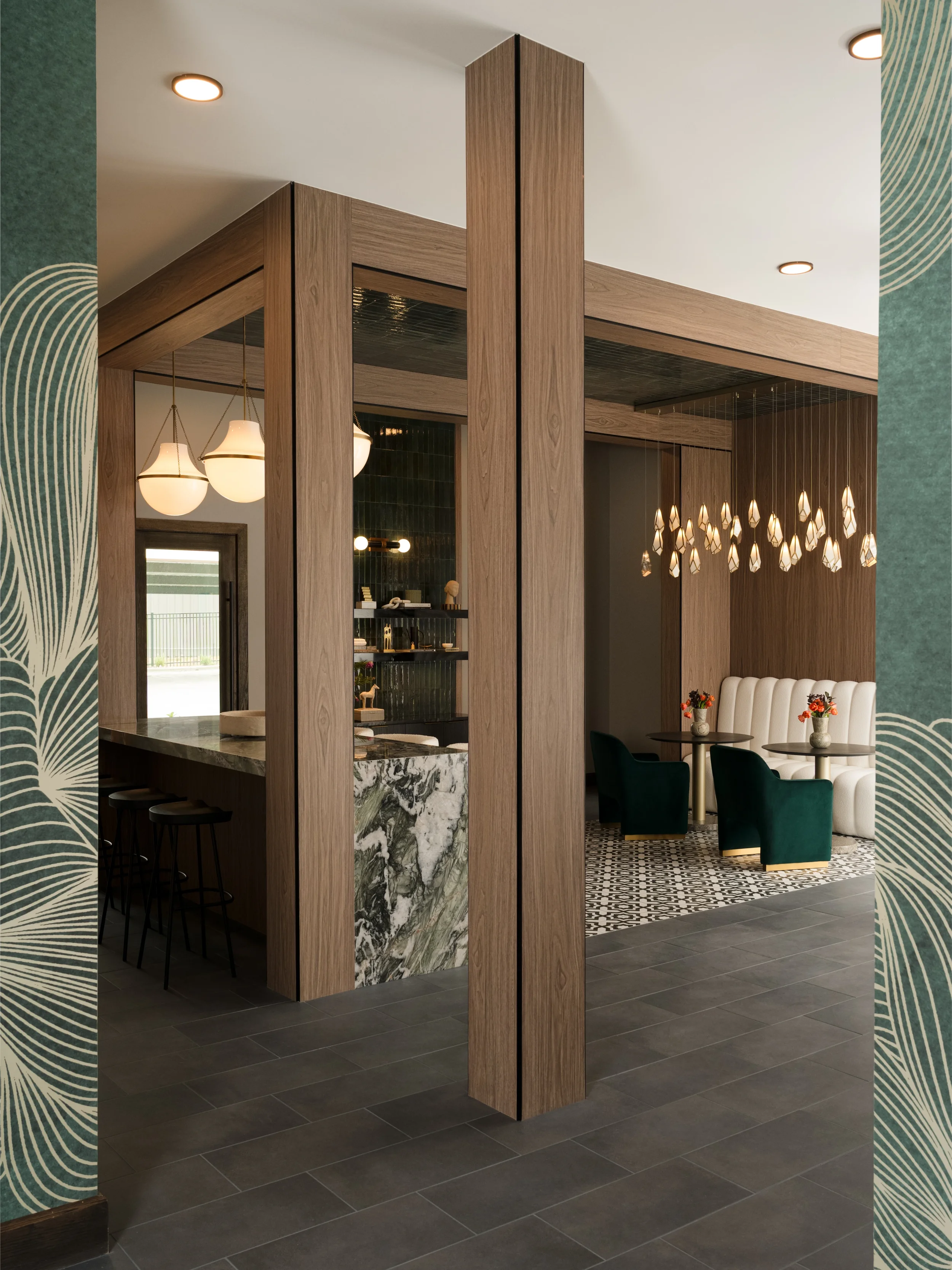 Walnut-framed opening between the bar and lounge at The Platform in Frisco, Texas, with a marble waterfall counter, glass pendants, and a channel-tufted banquette, designed by Artbuckle & Co.