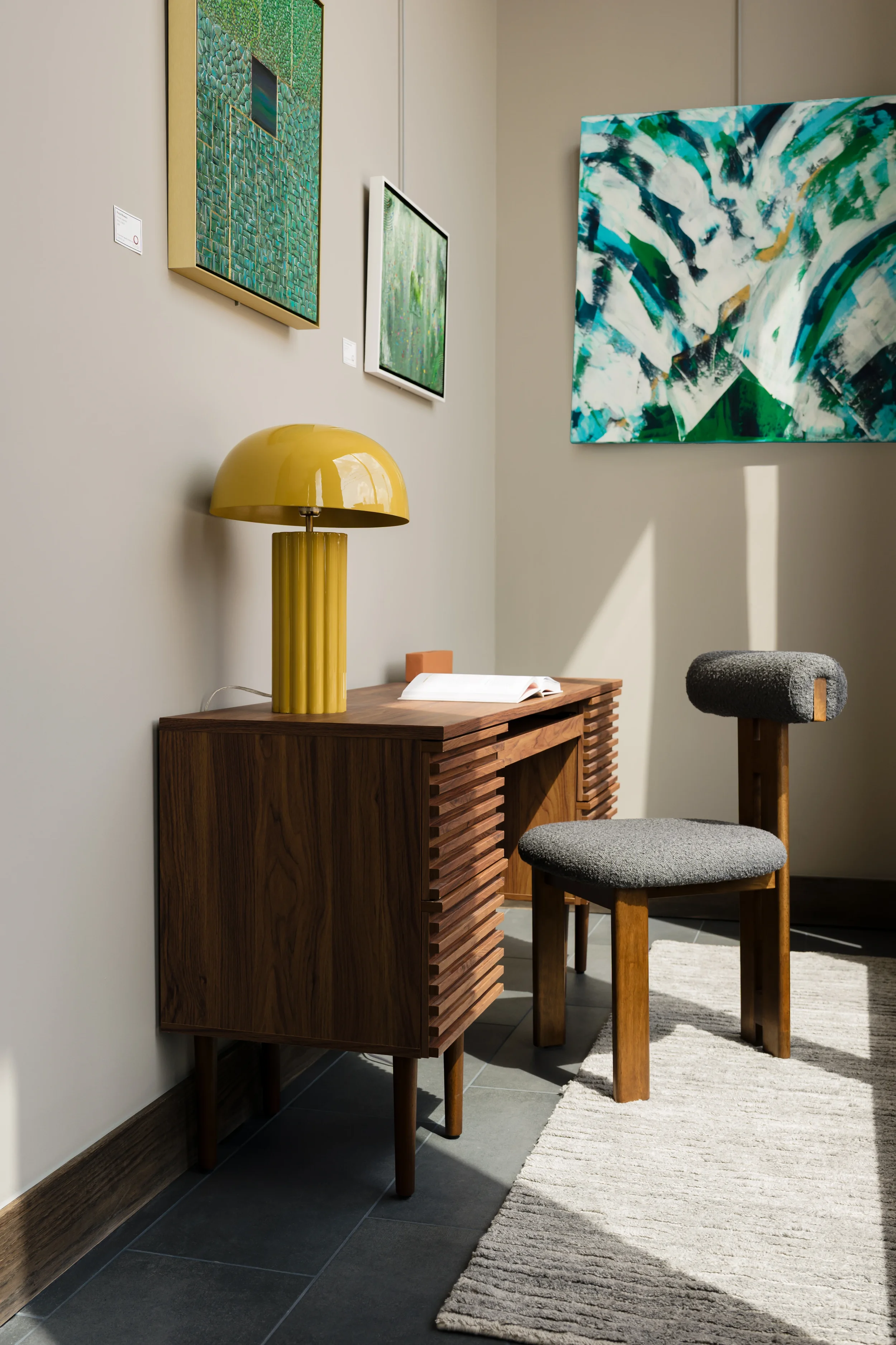 Work nook at The Platform in Frisco, Texas, with a walnut slatted desk, a yellow ribbed lamp, a bouclé stool, and abstract art, designed by Artbuckle & Co.