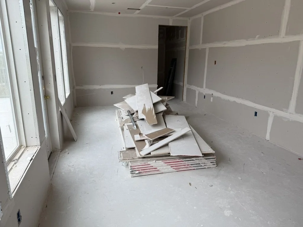 Before view of the resident amenity lounge during construction at Gateway Park apartments in Dallas, TX, showing unpainted drywall and a stack of drywall sheets before interior buildout by Artbuckle & Co.