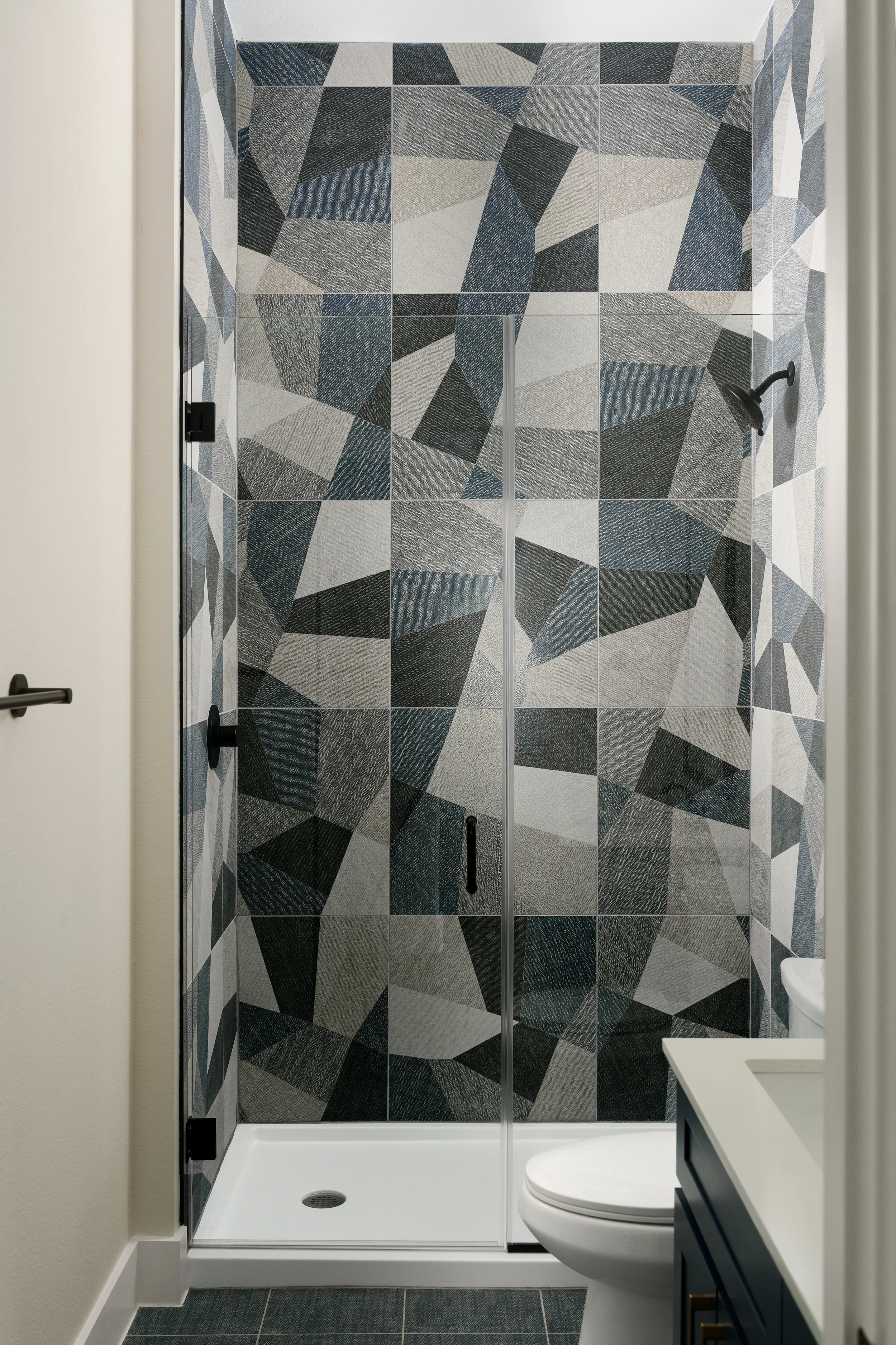 Apartment shower at The View in Frisco's Rail District with geometric blue and gray tile. Designed by Artbuckle & Co.