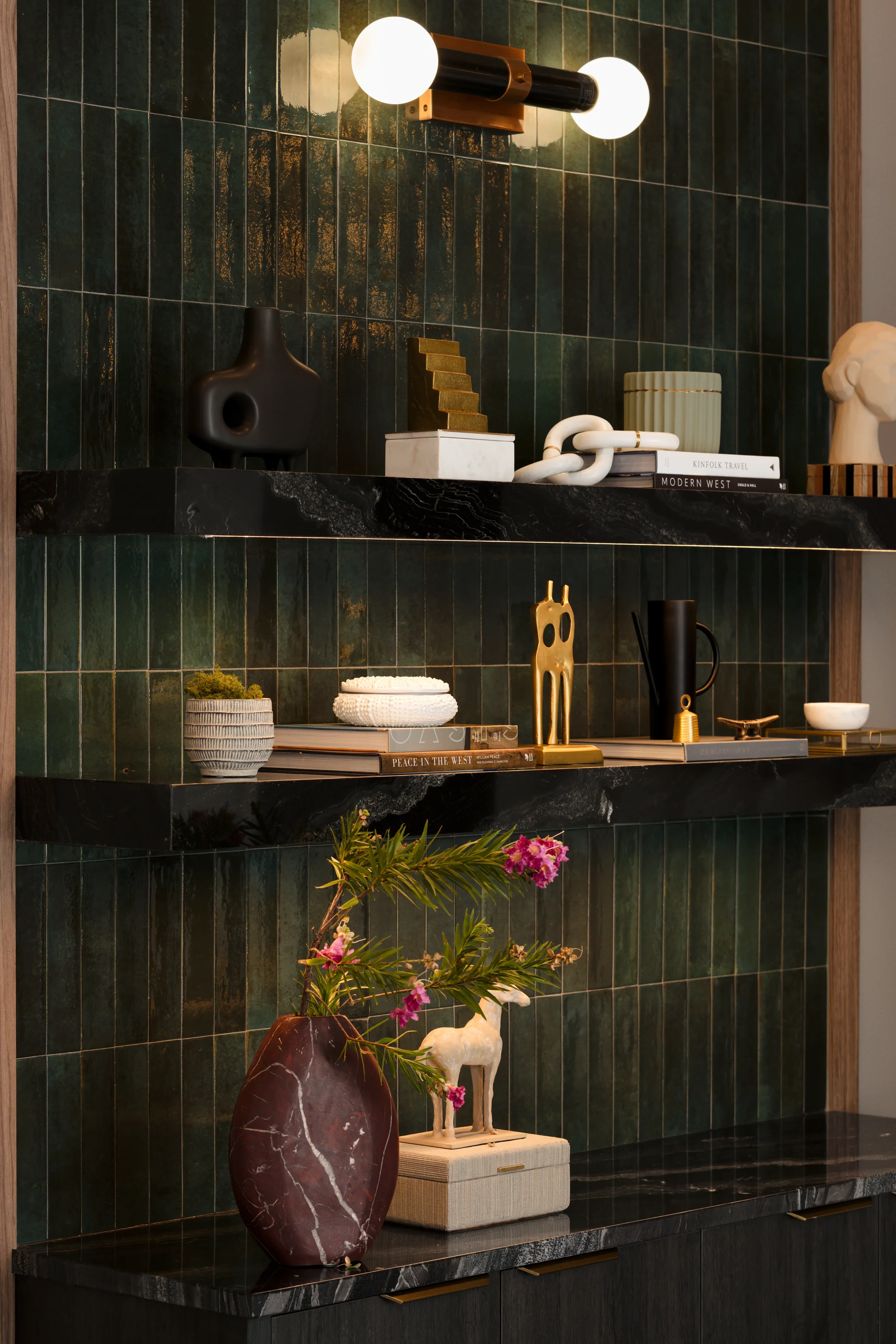 Floating black stone shelves on green zellige tile, styled with sculptural objects, at The Platform in Frisco, Texas, designed by Artbuckle & Co.