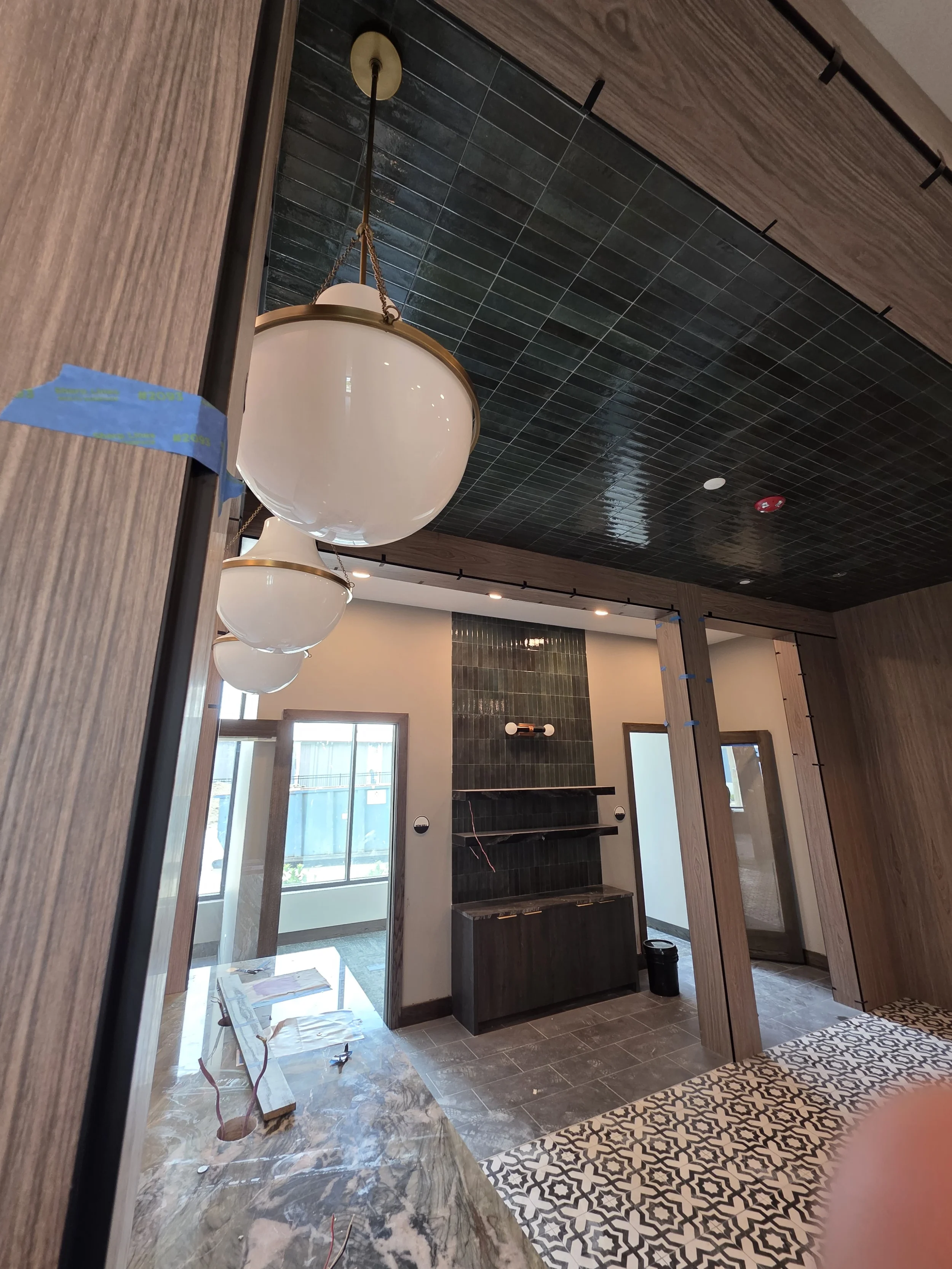 Lobby in progress at The Platform in Frisco, TX with globe pendants, walnut trim and green tile ceiling. Designed by Artbuckle & Co.