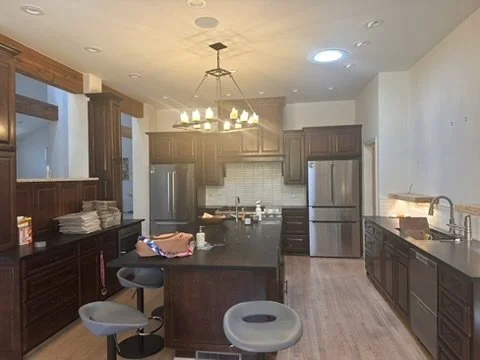 Before: the Lakewood Hills kitchen in Dallas, Texas, with dark wood cabinetry, a black-topped island, stainless steel refrigerators, and an iron chandelier, prior to the Artbuckle & Co. renovation.