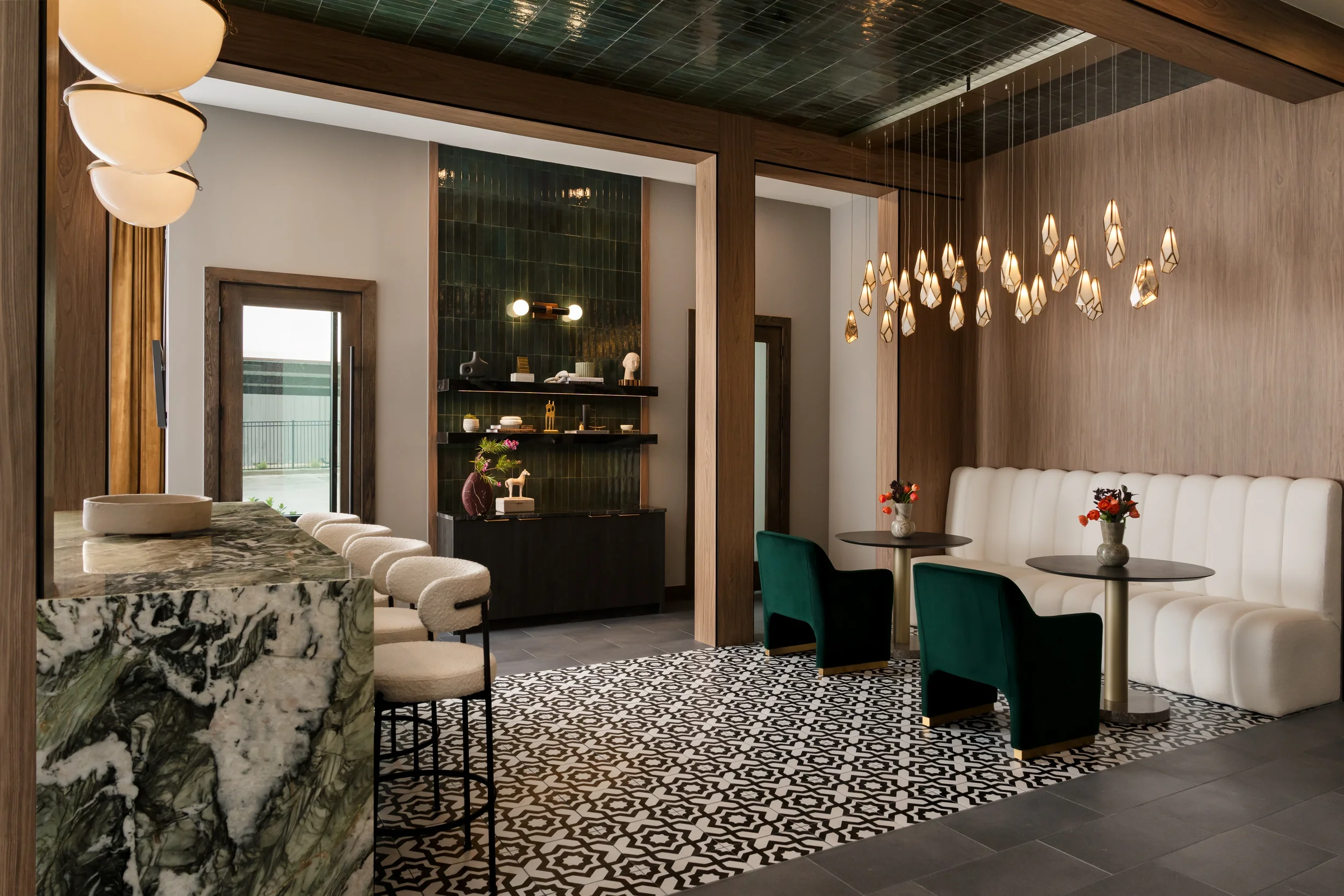 Amenity bar at The Platform in Frisco, Texas, with a marble waterfall counter, bouclé stools, green velvet chairs, and a pendant cluster over graphic tile, designed by Artbuckle & Co.