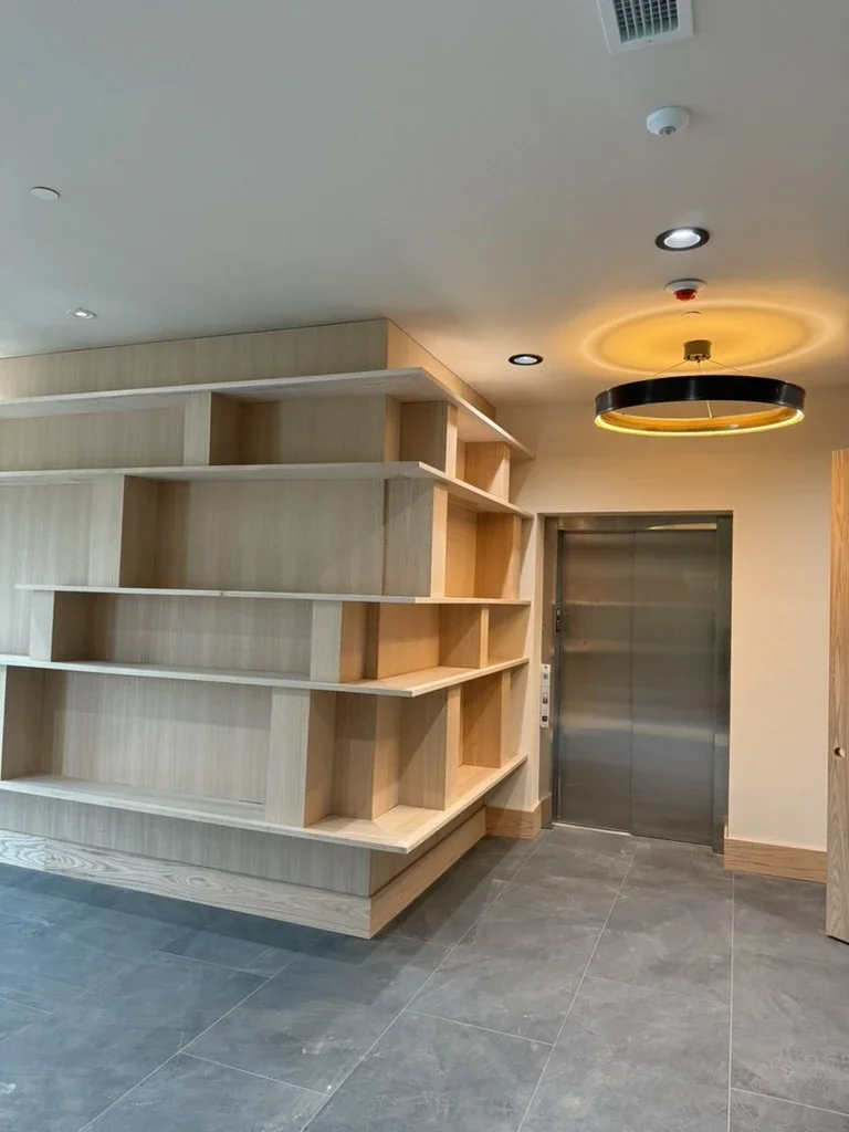 Oak shelving wall beside the elevator at The View in Frisco's Rail District with a glowing ring light fixture.