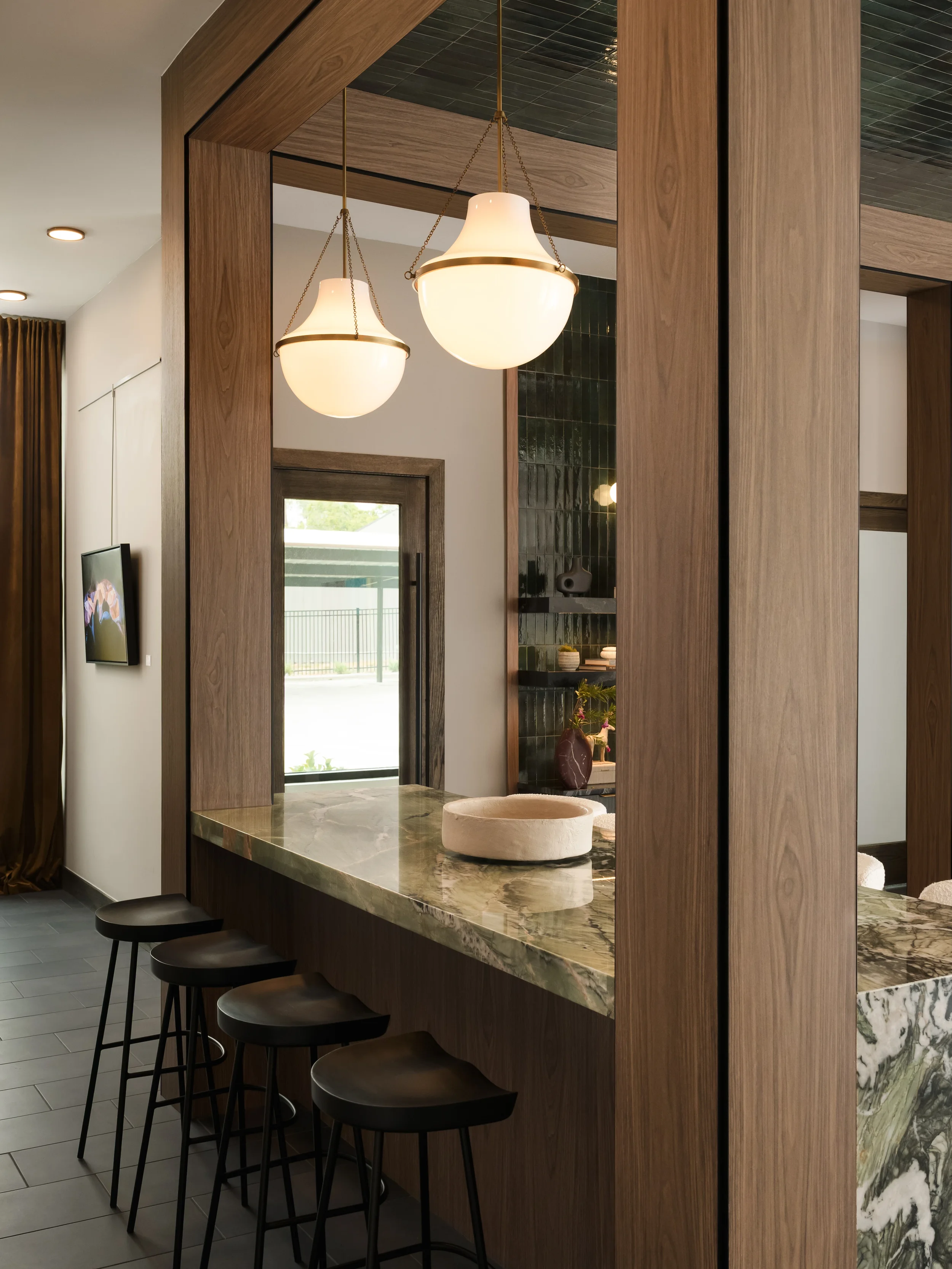 Marble-topped amenity bar with black stools and globe pendants framed by walnut paneling at The Platform in Frisco, Texas, designed by Artbuckle & Co.