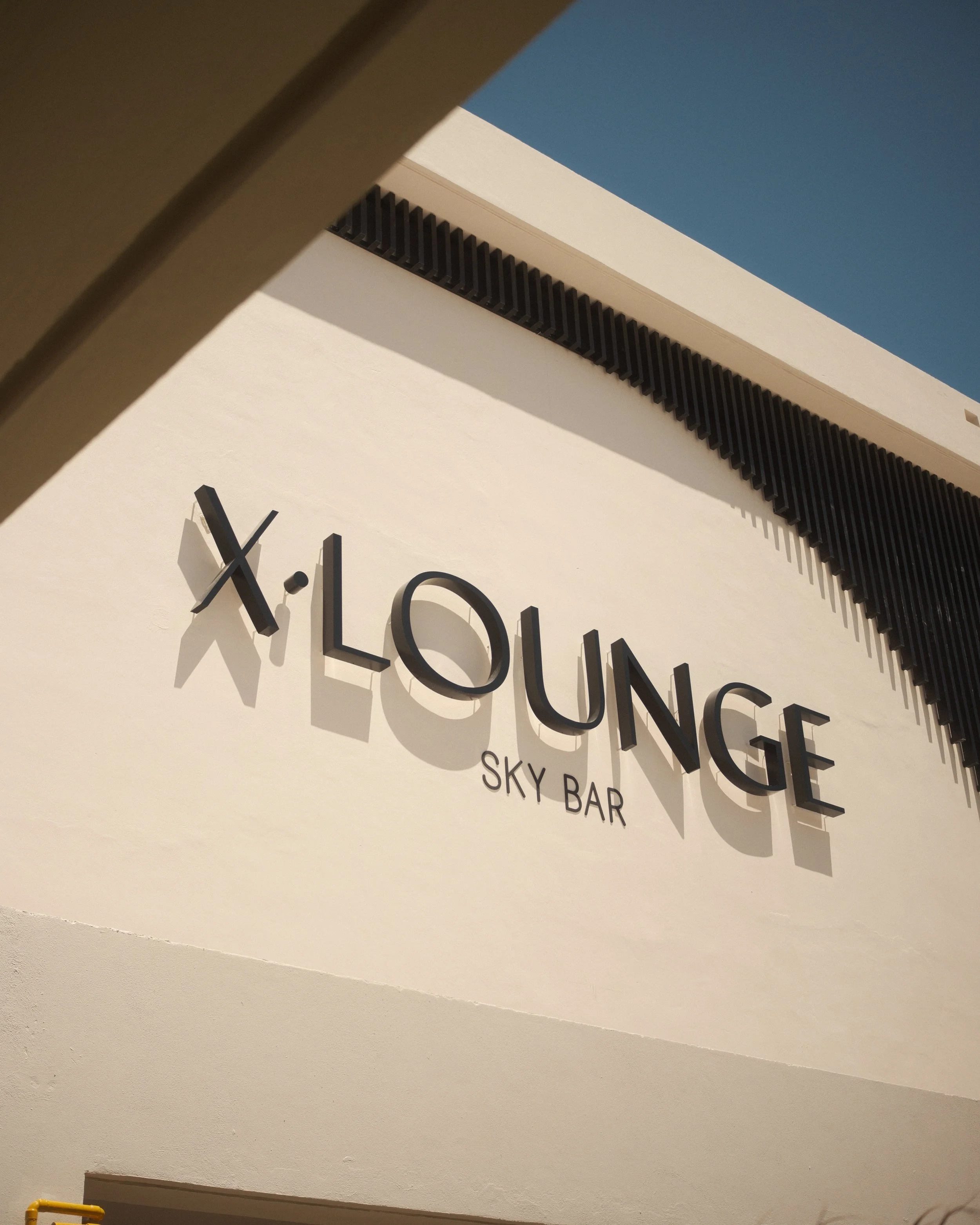 Sign reading 'X Lounge Sky Bar' on a white building under a clear blue sky, in Cancun Mexico.