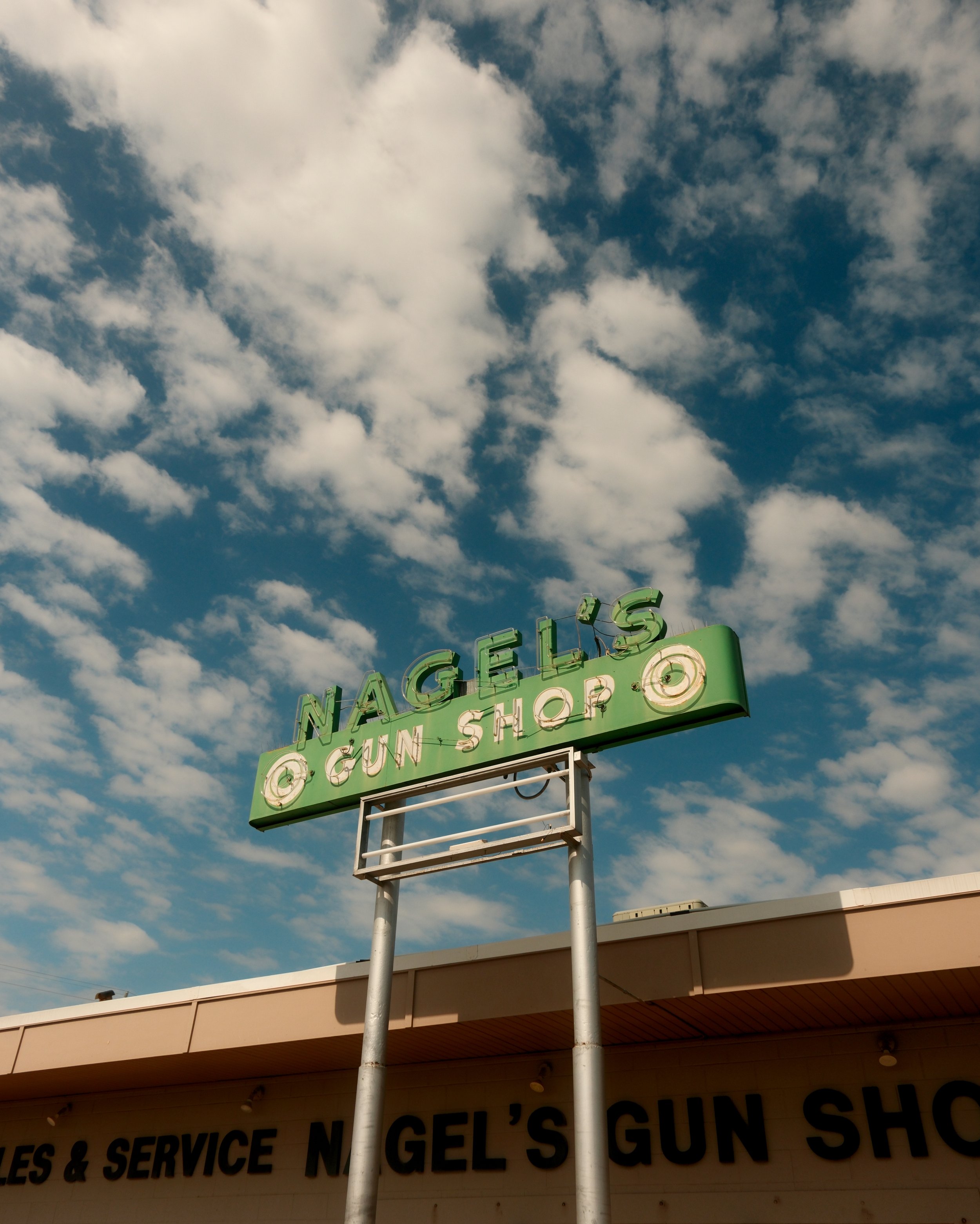 Neon sign for Nagel's Gun Shop against a partly cloudy sky