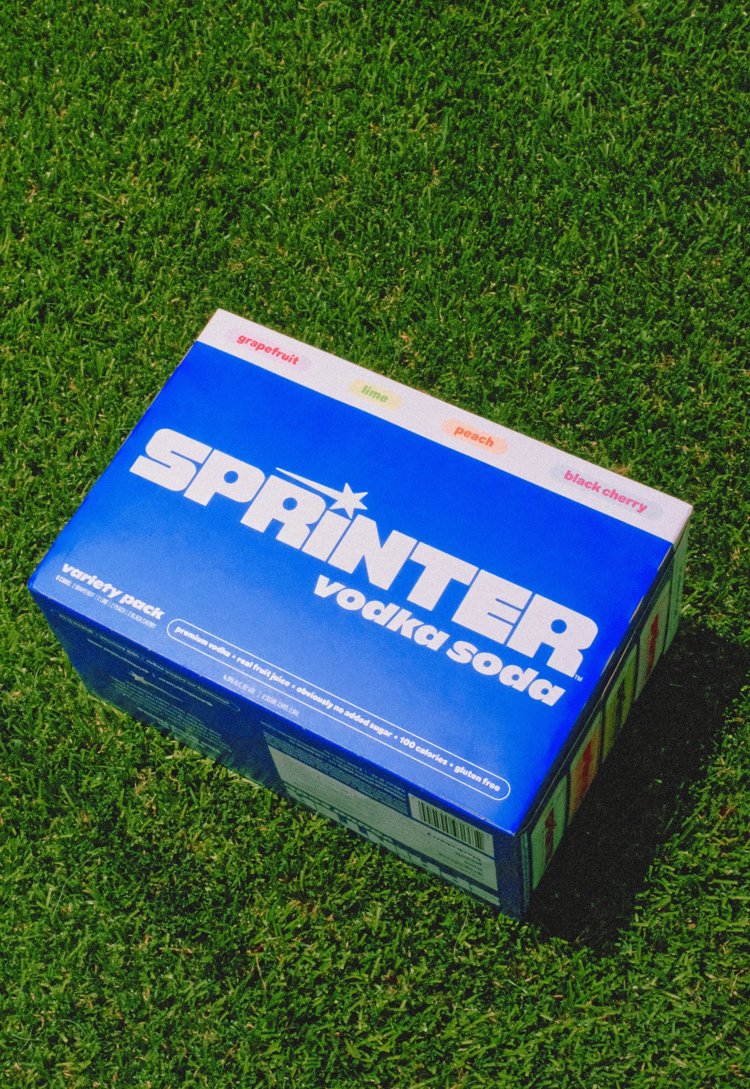 A blue box of Spindrift soda on grass, flavor options listed at the top include grapefruit, lime, peach, and black cherry.