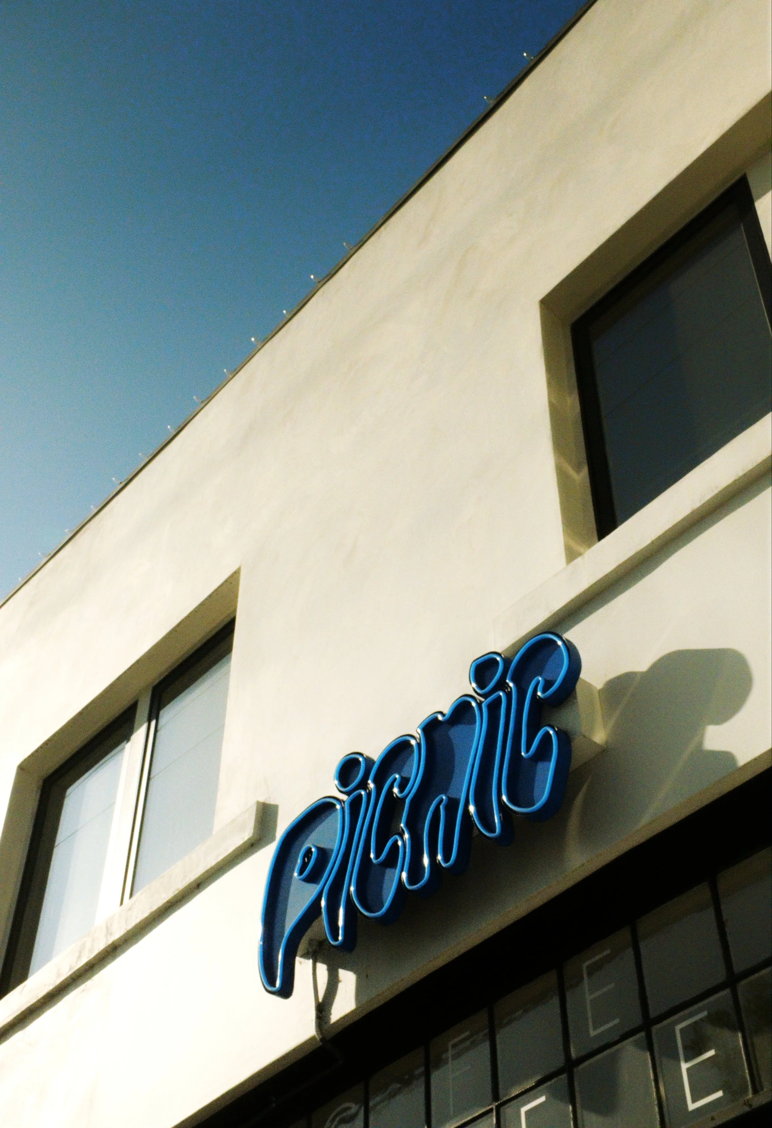 A white building with two rectangular windows and a blue neon sign that reads 'Cicicino' on the exterior wall.