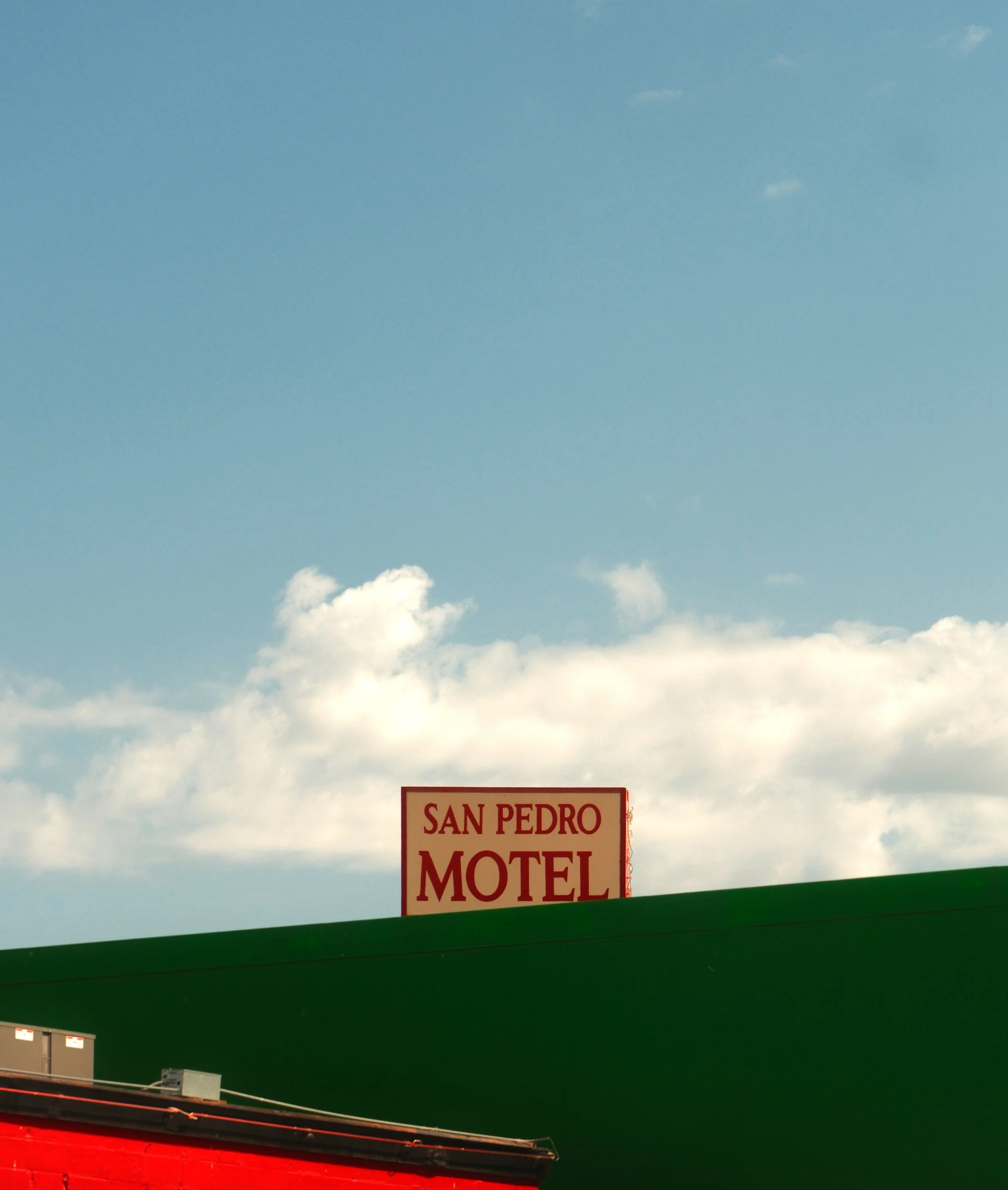 Sign on a building that reads 'San Pedro Motel' against a blue sky with clouds.