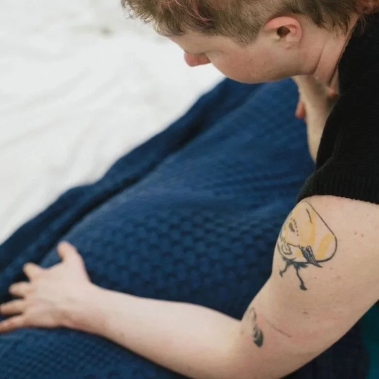 Close-up of a person with short curly hair, wearing a black shirt, showing a large tattoo on their upper arm.