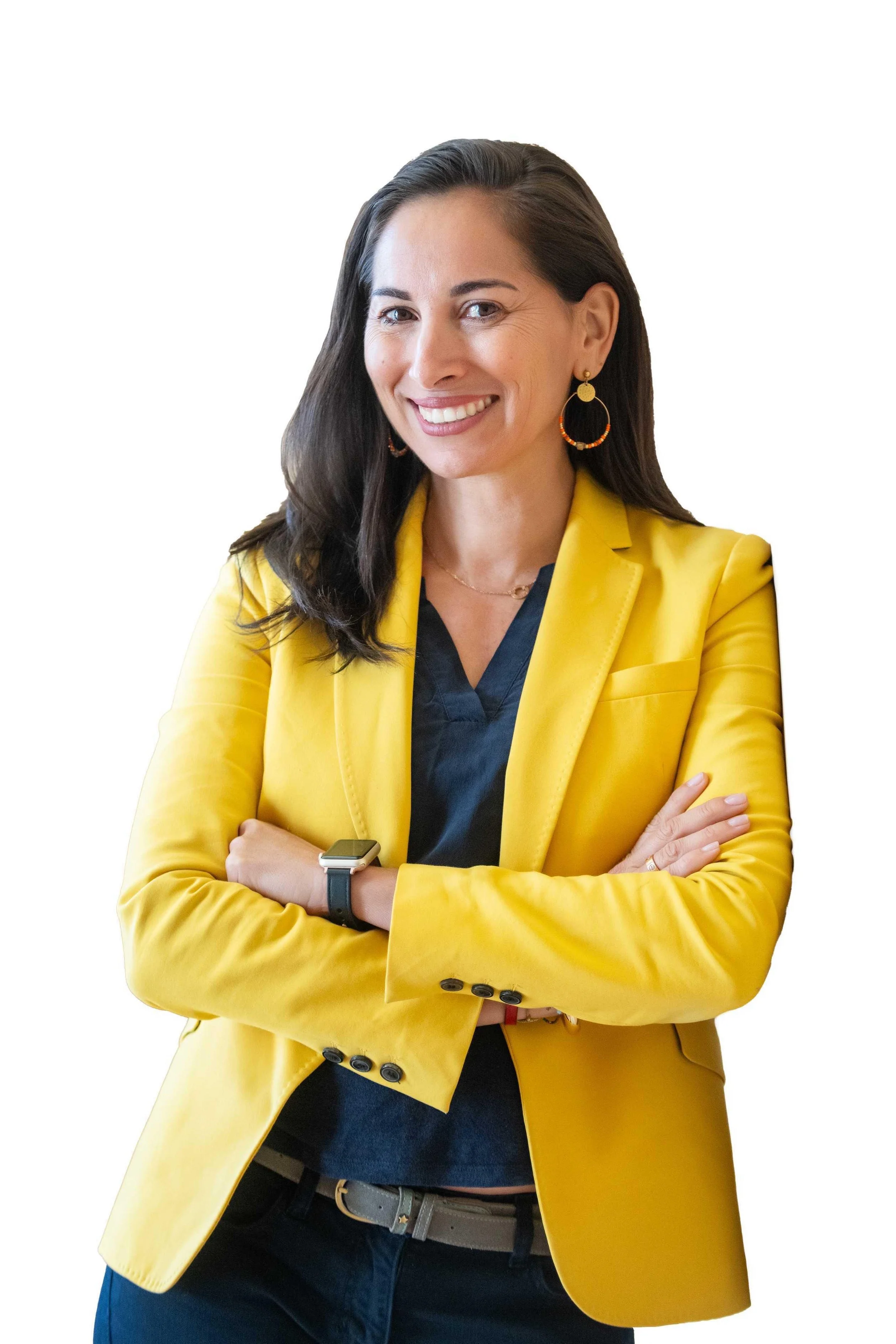 A woman with dark brown hair wearing a yellow blazer, black top, and earrings, smiling with arms crossed, against a white background.