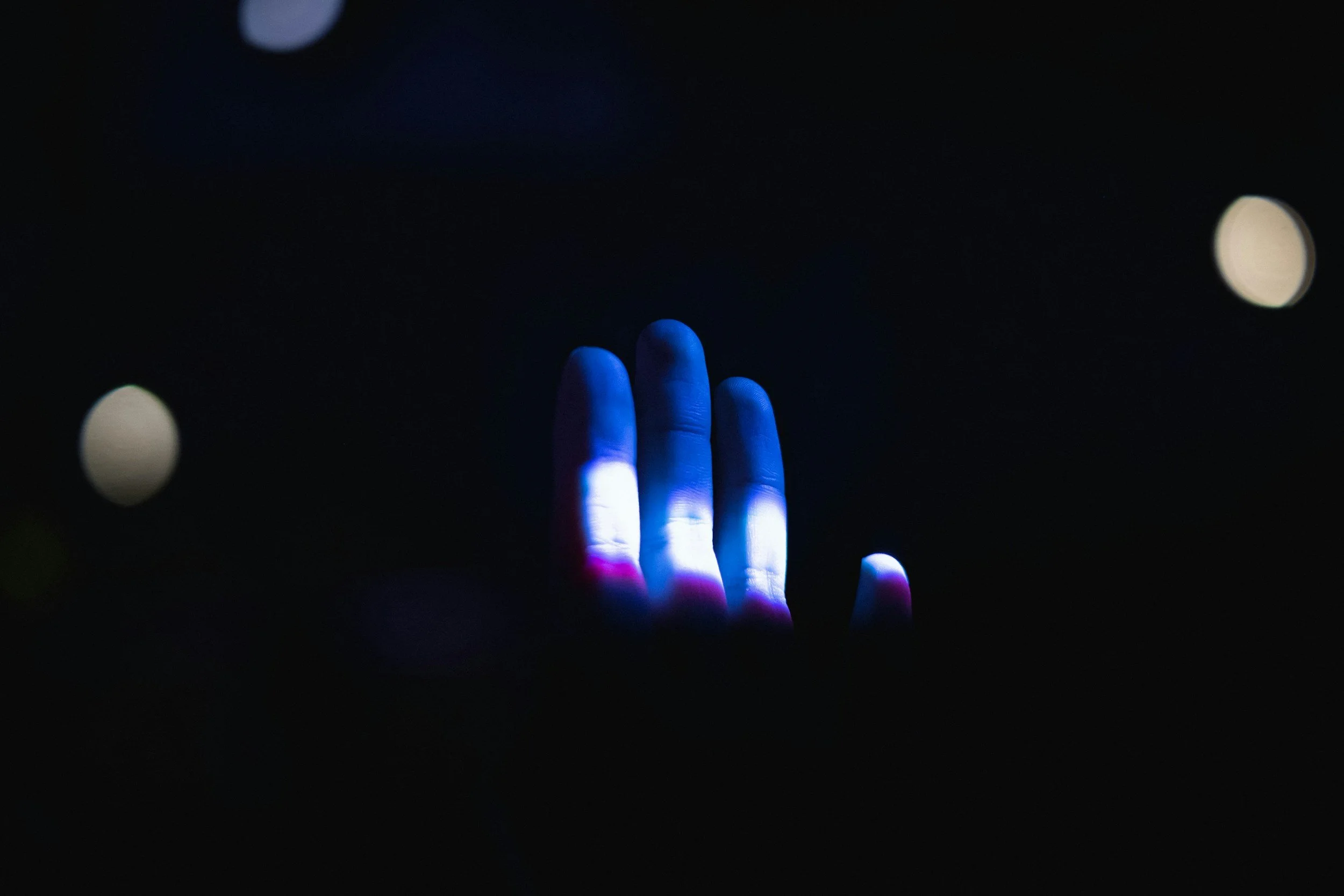 A hand illuminated by blue, white, and pink light against a dark background, with blurred light orbs surrounding it.